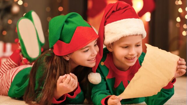 Children clad in Christmas attire examining a scroll.