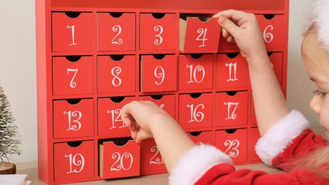 A child in festive Christmas attire opening advent calendar compartments.