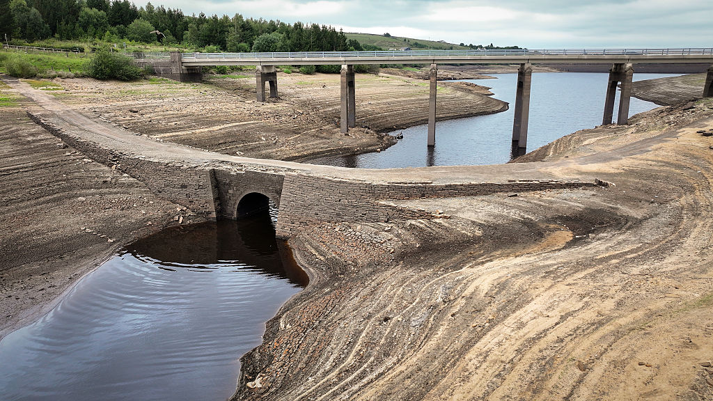 a water reservoir has water levels so low that an ancient pack horse bridge is exposed in the foreground