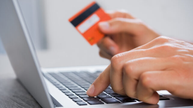 Hands holding a credit card while typing on a laptop