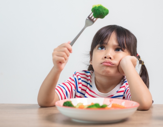 A confused or grumpy child holding broccoli on a fork