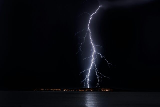 Single lightning bolt arcing to ground through night (black) sky.
