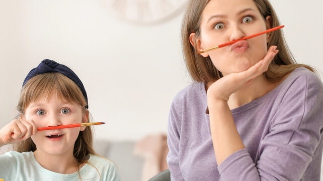 A mother and child being silly with pens balanced on their lips