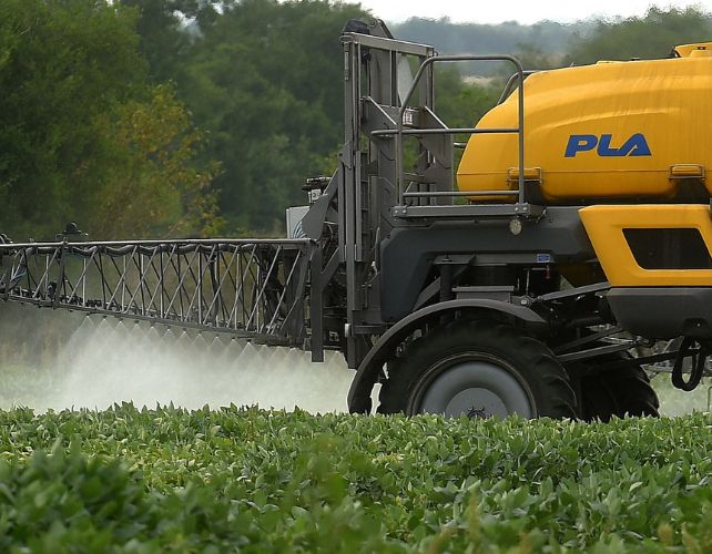 an industrial-size tractor fumigates a field of soybeans with a fine mist