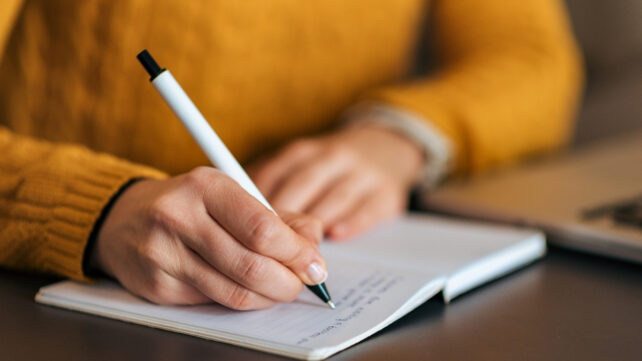 A person wearing a yellow sweater is writing in a notebook