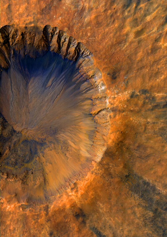 This image of an impact crater in the Sirenum Fossae region of Mars was taken by NASA’s Mars Reconnaissance Orbiter on March 30, 2015. The crater is approximately 3,300 feet (1-km) wide and appears relatively recent as it has a sharp rim and well-preserved ejecta. The steep inner slopes are carved by gullies and include possible recurring slope lineae on the equator-facing slopes. Image credit: NASA / JPL / University of Arizona / Alfred McEwen.