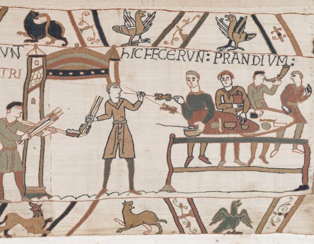 a scene in the bayeux tapestry showing three soldiers feasting merrily at a table. to the left, a servant offers roast meat on long sticks. to the right, one soldier blows a horn.