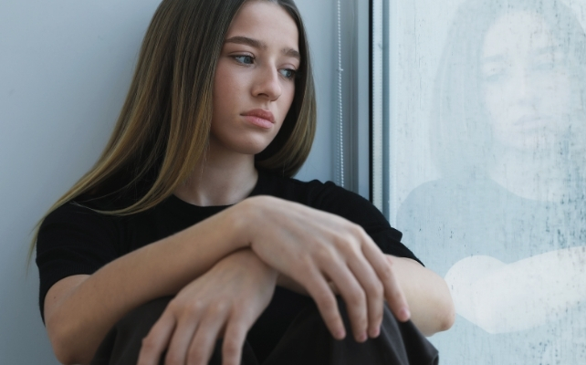 girl depressed sitting next to a window