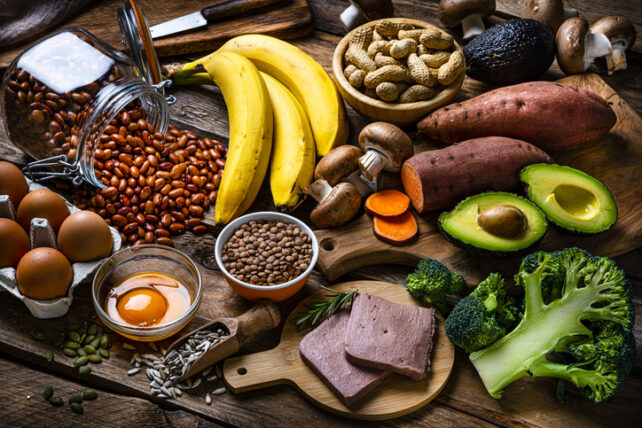 An assortment of foods rich in vitamin B6, including various meats, eggs, bananas, broccoli, sunflower seeds, legumes, avocados, mushrooms, peanuts, and sweet potatoes