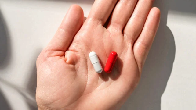 Woman's hand holding red pills against white table at home. Close-up.