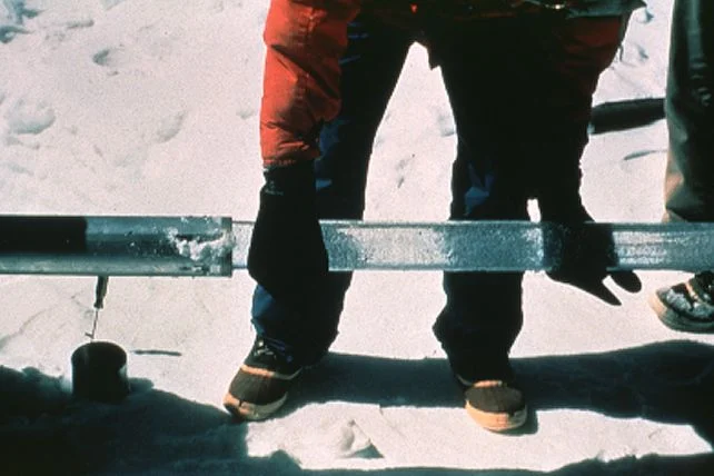 Scientists extracting an ice core sample from a drill.