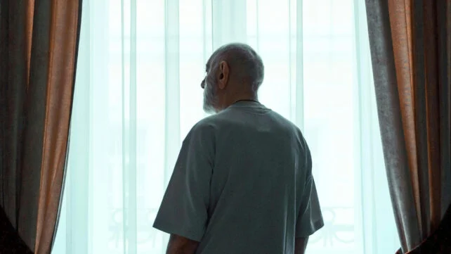 Older Man Standing by the Window Looking Outside